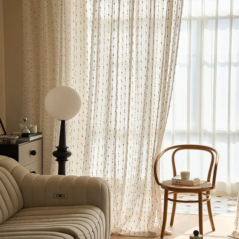Living room with beige sofa, wooden chair, and sheer curtains.
